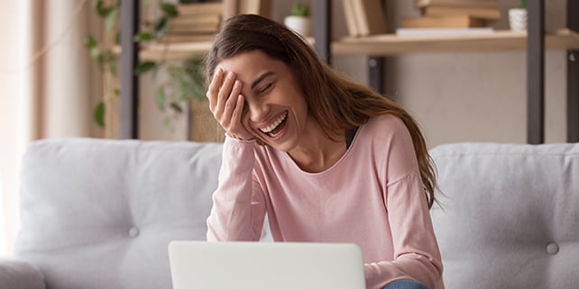 Frau sitzt vor Laptop während eines Video-Calls mit ihrer Mutter und lacht.