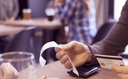 Im Bildausschnitt sieht man in einem Restaurant eine Hand, die eine Rechnung hält.