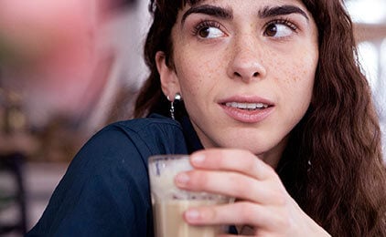 Frau schaut etwas skeptisch während sie einen Kaffee in der Hand hält