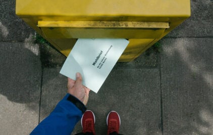 Ein Wahlbrief wird in einen Postkasten geworfen.