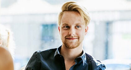 Männertypen symbolisch durch einen Mann der vor zwei Frauen sitzt und charmant lächelt