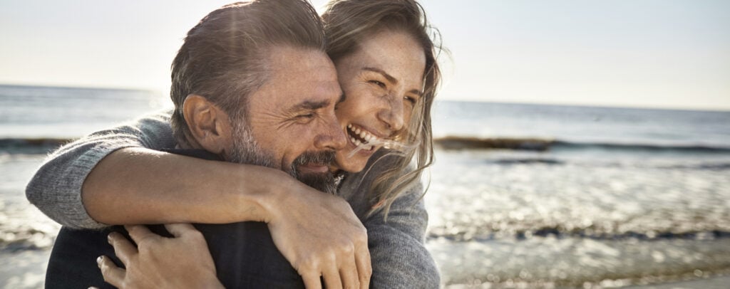 Ein Mann und eine Frau lachen gemeinsam, das Meer im Hintergrund.