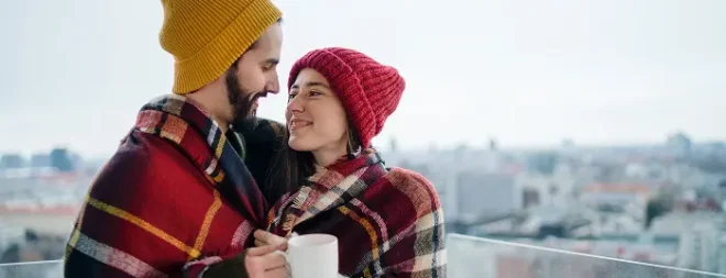 Paar kuschelt im Winter unter einer Decke und hält warme Teetassen in den Händen